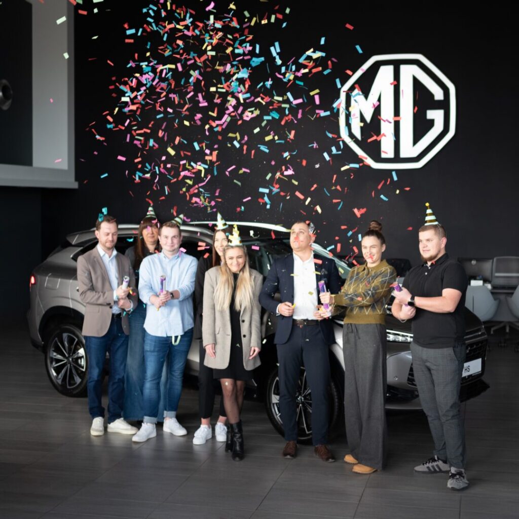 zespół MG na tle logo w salonie w urodzinowych nastrojach